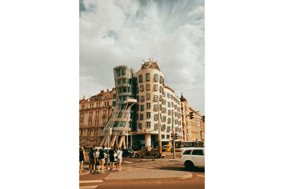 Un edificio dall'architettura decostruttivista, con una torre di vetro, si trova su una strada cittadina trafficata.