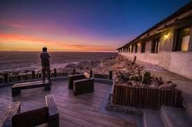 A person standing on a wooden deck of a building, looking out at the ocean during a colorful sunset.