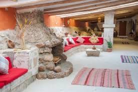 A rustic lounge area with a large stone fireplace, a curved red sofa, and a ceiling with exposed wooden beams.