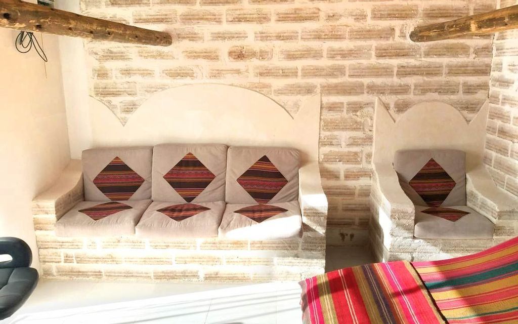 A rustic room interior with a sofa and armchair built into a light-colored brick wall, adorned with patterned cushions.