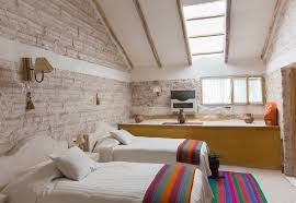 A rustic hotel room with two single beds, textured white brick walls, and a sloped ceiling with a skylight.