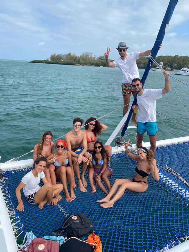 Amici in viaggio di gruppo WeRoad, sorridenti e in posa sulla rete di un catamarano in mare.