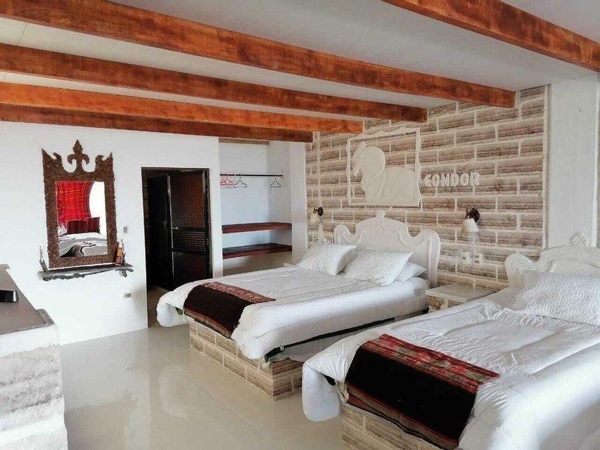 The interior of a hotel room with two beds, an accent wall made of salt bricks, and a ceiling with exposed wooden beams.