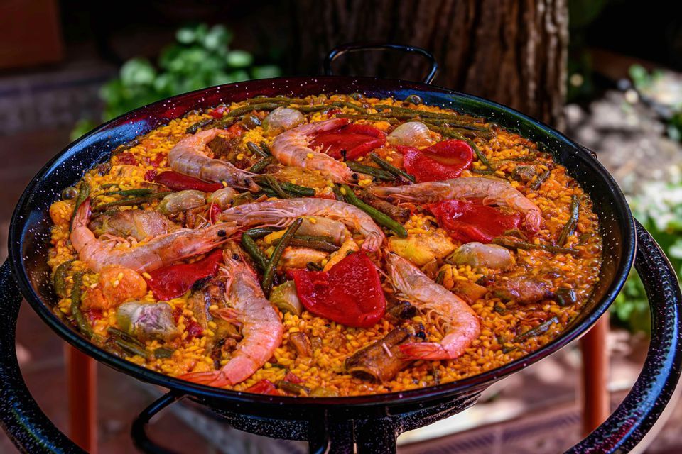 Un primo piano di una paella tradizionale in una grande padella nera, ricca di gamberi, peperoni rossi e fagiolini.