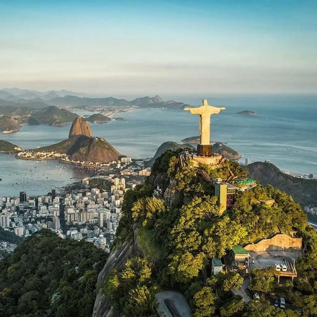 Veduta aerea della statua del Cristo Redentore su una montagna, con il Pan di Zucchero e una città costiera sullo sfondo.