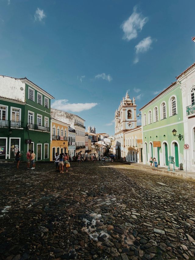 Una larga strada acciottolata, fiancheggiata da colorati edifici coloniali, con persone che passeggiano in una giornata di sole.