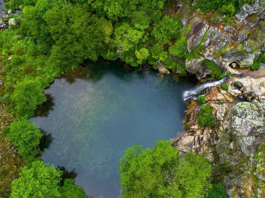 Vista aerea dall'alto di una cascata che si getta in una piscina naturale cristallina, circondata da una lussureggiante foresta verde e rocce.