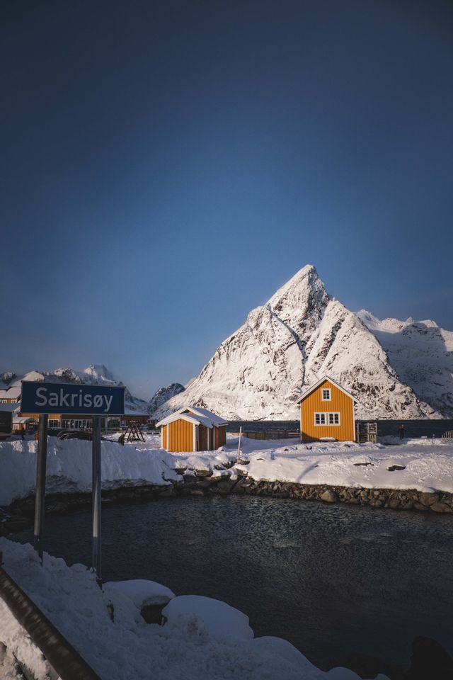 Un cartello stradale blu e baite gialle in un paesaggio innevato, davanti a una grande montagna innevata.