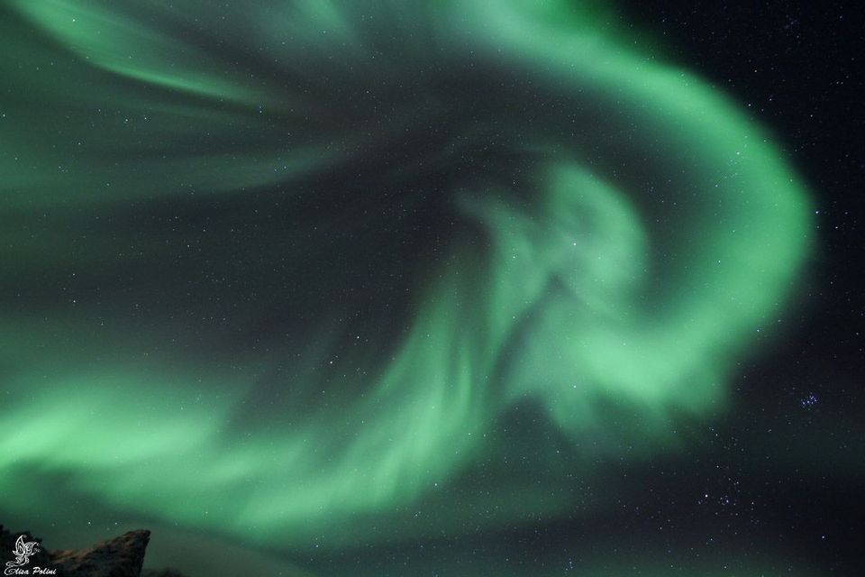 L'aurora boreale verde si libra in un cielo notturno buio e stellato, sopra una sagoma rocciosa all'angolo.