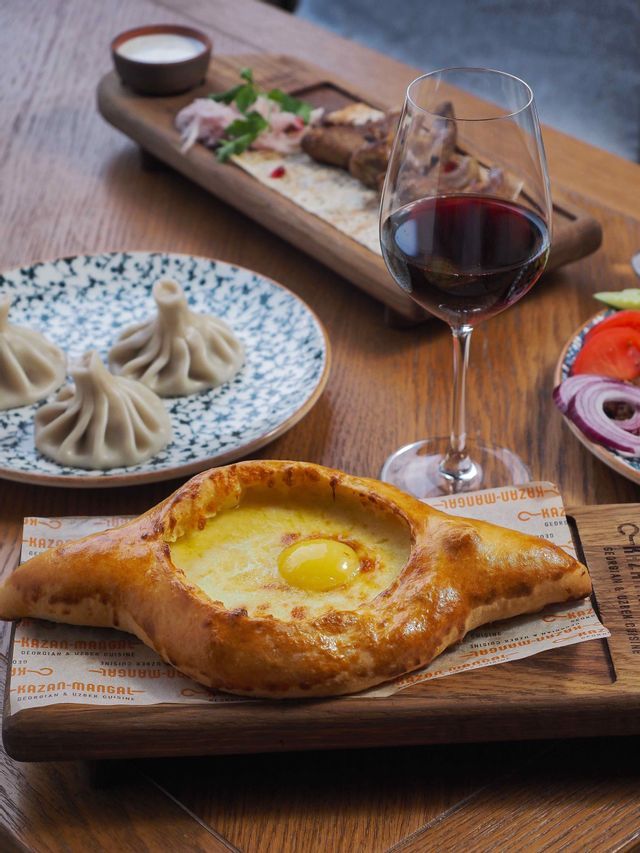 Un pasto tradizionale georgiano con Khachapuri Adjaruli, Khinkali e un bicchiere di vino rosso su un tavolo di legno.
