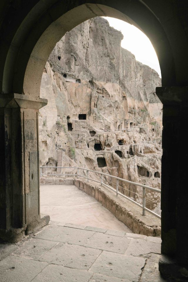 Una vista da un arco in pietra di numerose grotte artificiali scavate in un'imponente parete rocciosa.