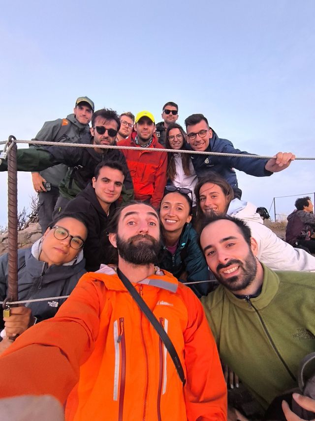 Un viaggio di gruppo WeRoad con persone sorridenti, in giacche da esterno, che posano per un selfie di gruppo su una collina.
