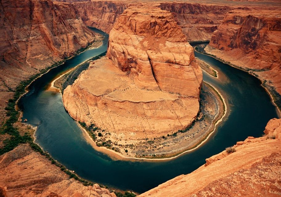 Veduta aerea di un fiume che si incurva a ferro di cavallo attorno a un grande faraglione di roccia rossa all'interno di un canyon.