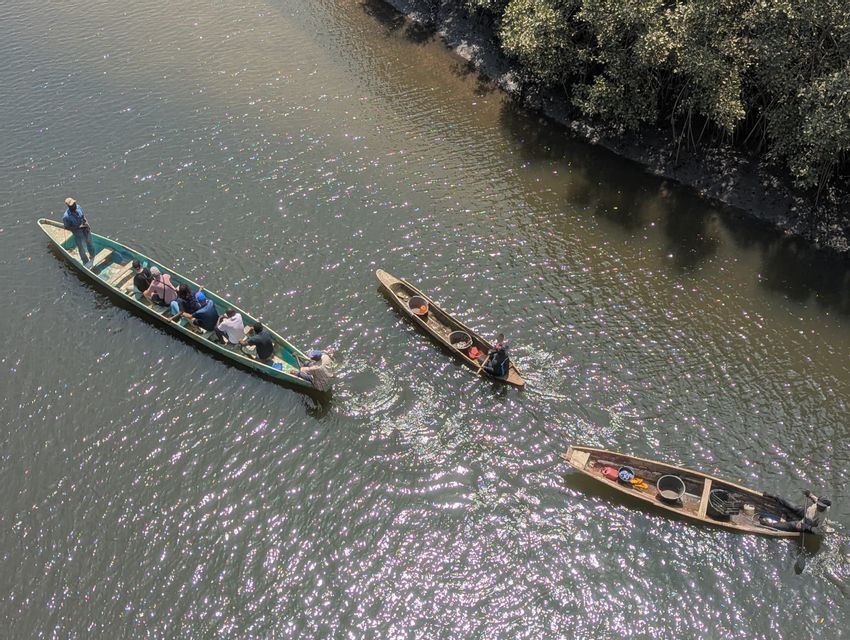 Una vista aerea di un viaggio di gruppo WeRoad su un'imbarcazione tradizionale su un fiume scintillante, con due canoe locali più piccole nelle vicinanze.