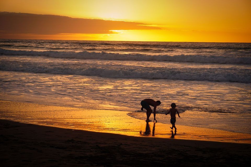 Un adulto e un bambino in silhouette giocano su una spiaggia bagnata dall'oceano durante un tramonto dorato.