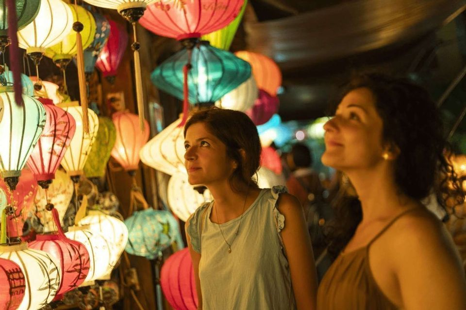 Due donne di un viaggio di gruppo WeRoad ammirano lanterne di carta colorate e illuminate appese in un mercato notturno.
