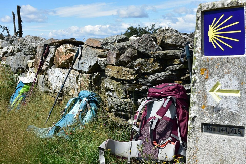 Zaini e bastoncini da trekking poggiano contro un muro di pietra accanto a un segnavia del Cammino di Santiago.