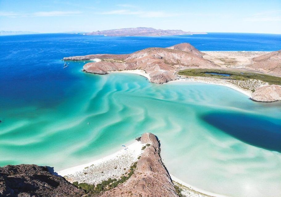 Una vista aerea di una costa rocciosa con spiagge di sabbia bianca, circondata da acque turchesi e dal blu intenso del mare.