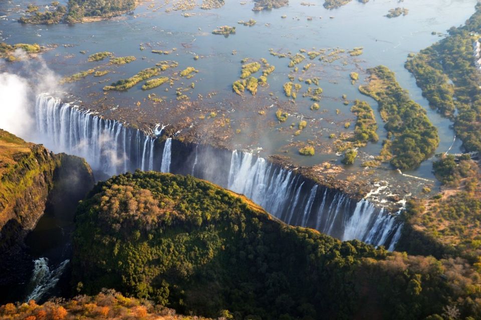 Eine Luftaufnahme eines gewaltigen Wasserfalls, der über eine breite, lange Schlucht stürzt, umgeben von einer üppigen grünen und braunen Landschaft.