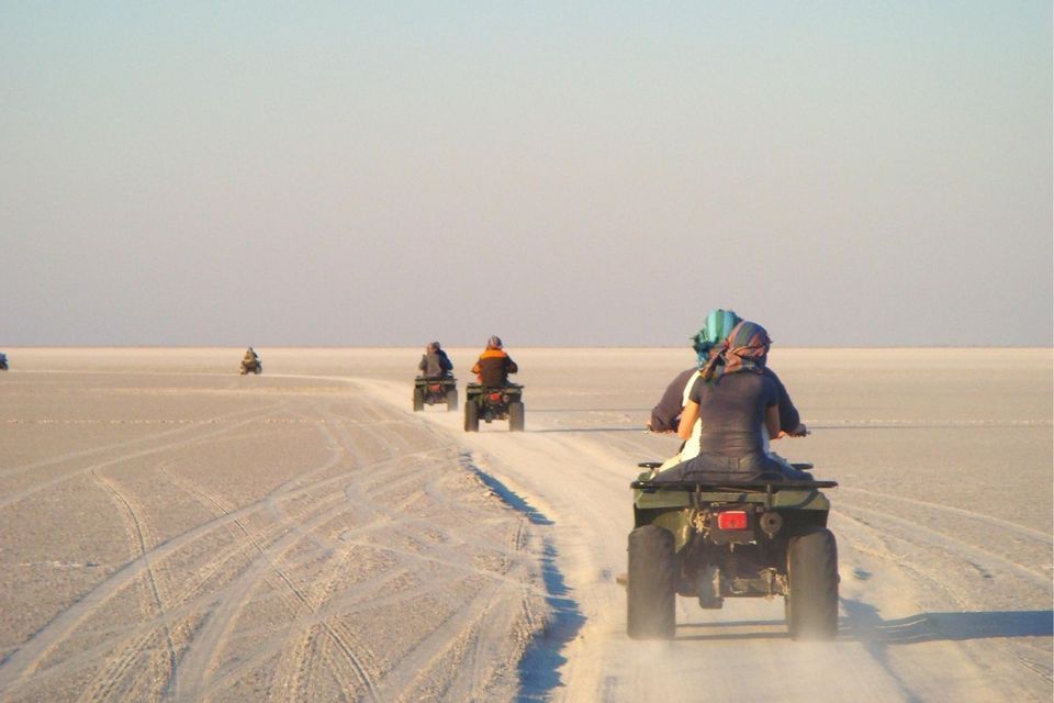 Eine WeRoad-Gruppenreise mit Quad-Bikes, die in einer Reihe über eine weite, weiße Salzpfanne unter klarem Himmel fahren.