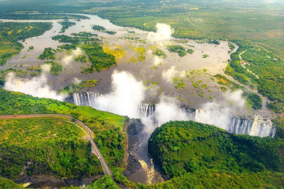 Luftaufnahme eines gewaltigen Wasserfalls an einem breiten Fluss, der in eine tiefe Schlucht stürzt und Nebelwolken über einer grünen Landschaft bildet.