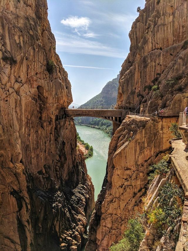 Un gruppo WeRoad cammina lungo uno stretto ponte e una passerella, intagliati nelle pareti rocciose a strapiombo di un profondo canyon sopra un fiume.