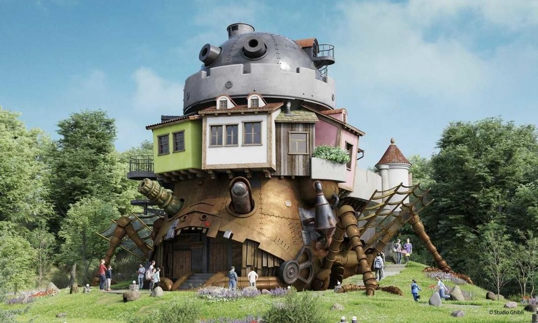 Un modello a grandezza naturale di un fantastico castello meccanico in movimento con case in cima, situato su una collina erbosa circondata da alberi e persone.