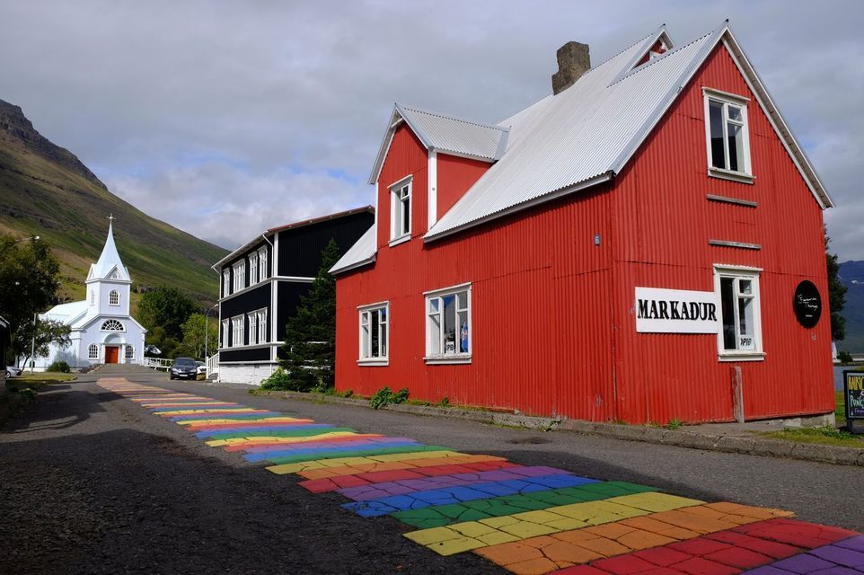 Une rue avec un chemin arc-en-ciel peint longe des bâtiments colorés et mène à une église blanche au pied d'une montagne.