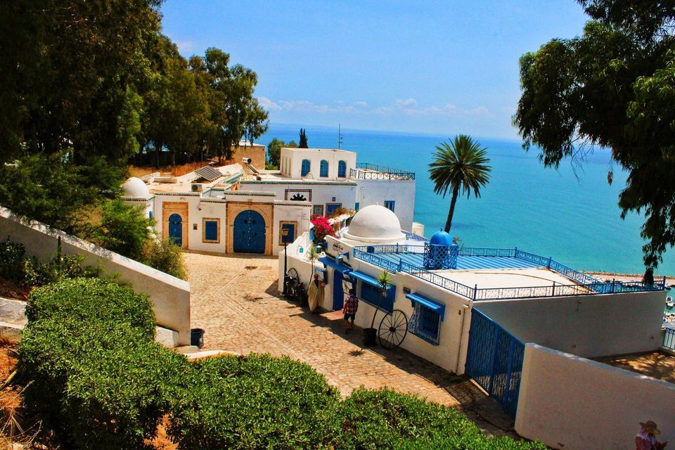 Un borgo di edifici bianchi con porte e finiture blu su una strada di ciottoli, arroccato su una scogliera a picco sull'oceano.