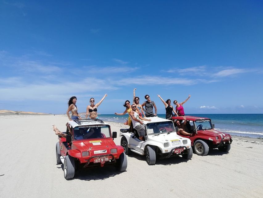 A WeRoad group trip posing on three off-road vehicles on a sandy beach with the ocean and a blue sky in the background.