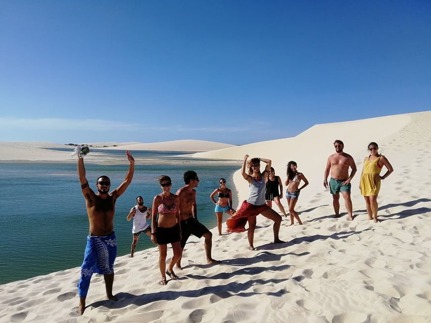 Un viaje en grupo de WeRoad posando en una duna de arena blanca junto a una laguna turquesa bajo un cielo despejado y soleado.