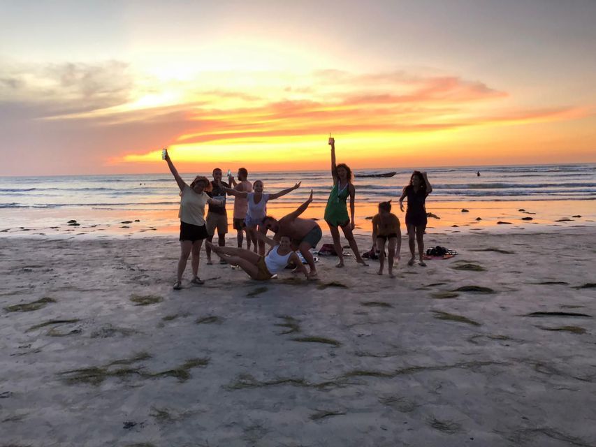 Un viaggio di gruppo WeRoad con persone che posano scherzosamente su una spiaggia sabbiosa con l'oceano alle spalle durante un tramonto colorato.