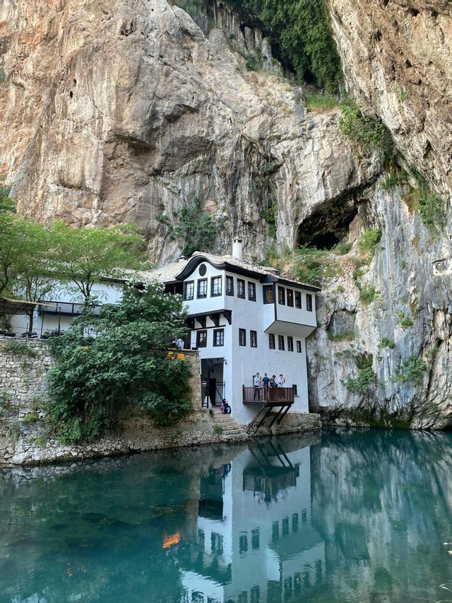 Un tradizionale edificio bianco costruito alla base di una ripida scogliera rocciosa, con il suo riflesso visibile nelle calme acque turchesi sottostanti.