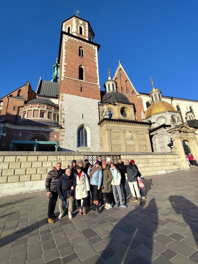 Un grupo de WeRoad posa para una foto en una plaza adoquinada frente a una gran catedral de ladrillo bajo un cielo azul claro.
