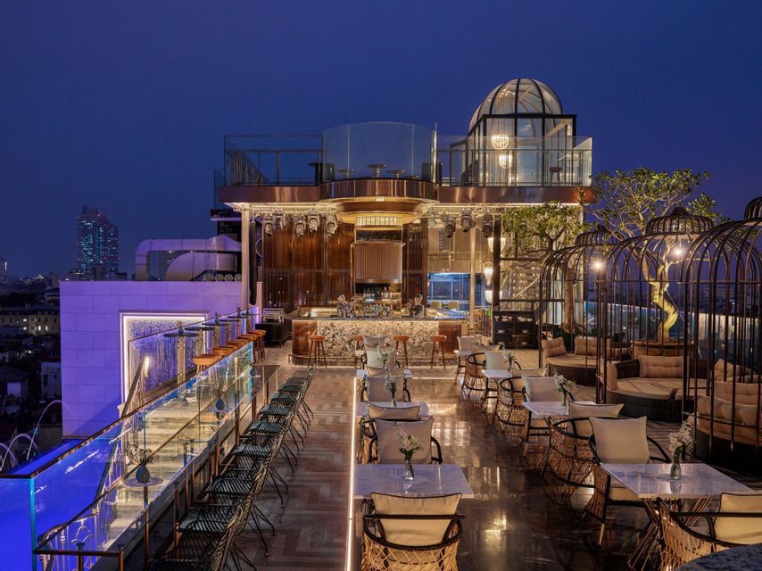 Un rooftop bar di lusso, vuoto e illuminato al tramonto, con un lungo bancone in marmo, sedute moderne e vista sullo skyline cittadino.