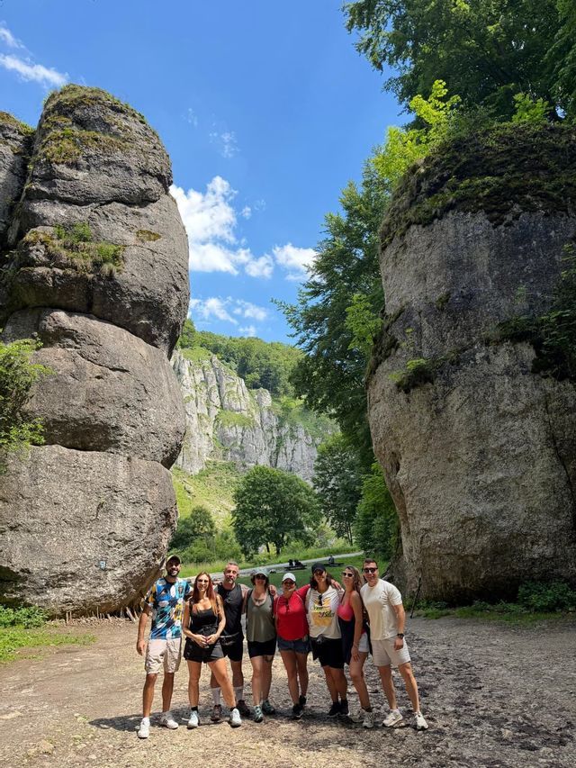 Un viaje en grupo de WeRoad posa para una foto en un sendero de tierra entre dos grandes formaciones rocosas cubiertas de musgo bajo un cielo azul.