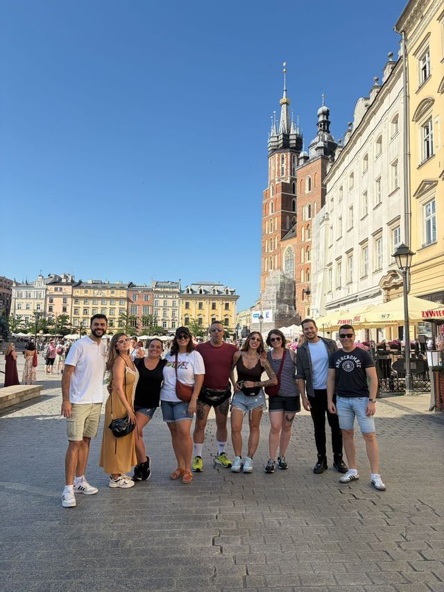 Un viaje en grupo de WeRoad de ocho personas posando para una foto en una soleada plaza adoquinada de la ciudad con edificios históricos al fondo.