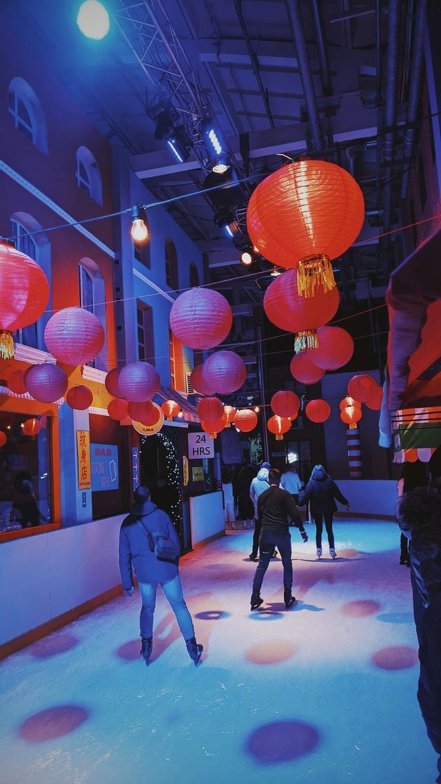Un viaggio di gruppo WeRoad per pattinare sul ghiaccio su una pista al coperto, illuminata da luci blu e viola e decorata con lanterne di carta rosse.
