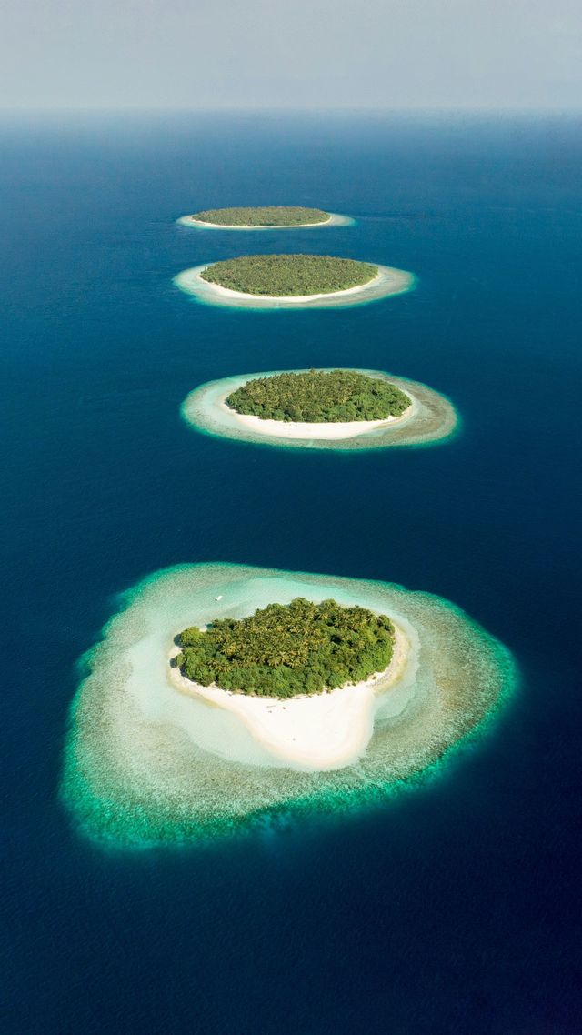 An aerial view of a line of small tropical islands with coral reefs surrounded by deep blue water.