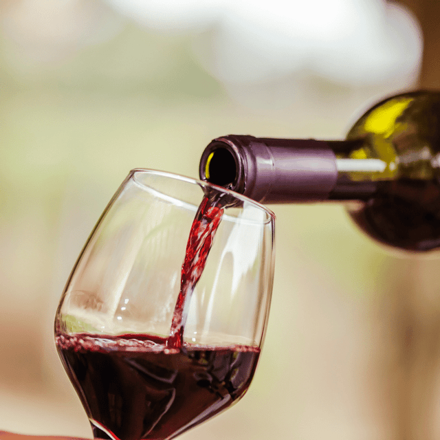 Un primo piano di vino rosso versato da una bottiglia in un bicchiere da vino su uno sfondo leggermente sfocato.