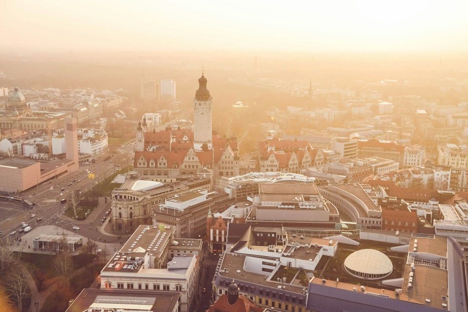Una vista aerea di una città europea con una torre storica centrale, immersa in una calda e dorata luce solare velata.