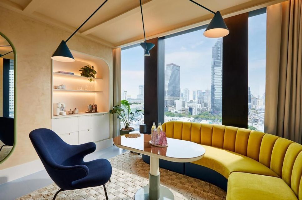 Un'area pranzo moderna con un divano curvo giallo e una poltrona blu che si affaccia su un panorama urbano attraverso una grande finestra.