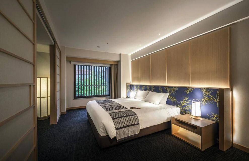 Interior of a modern hotel room with Japanese design elements, including a large bed, shoji screen, and a window with wooden blinds.