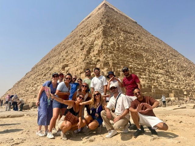 Un groupe WeRoad pose pour une photo devant une grande pyramide en pierre sous un ciel dégagé.
