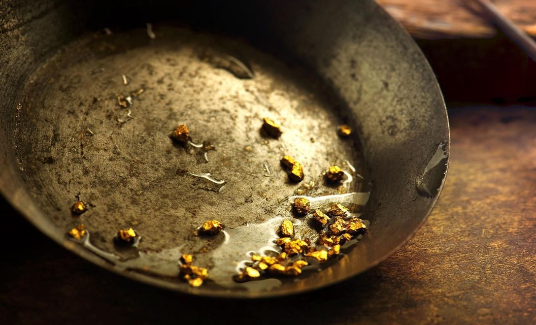 Un primo piano di piccole pepite d'oro che riposano con un po' d'acqua in una padella di metallo scura e usurata.