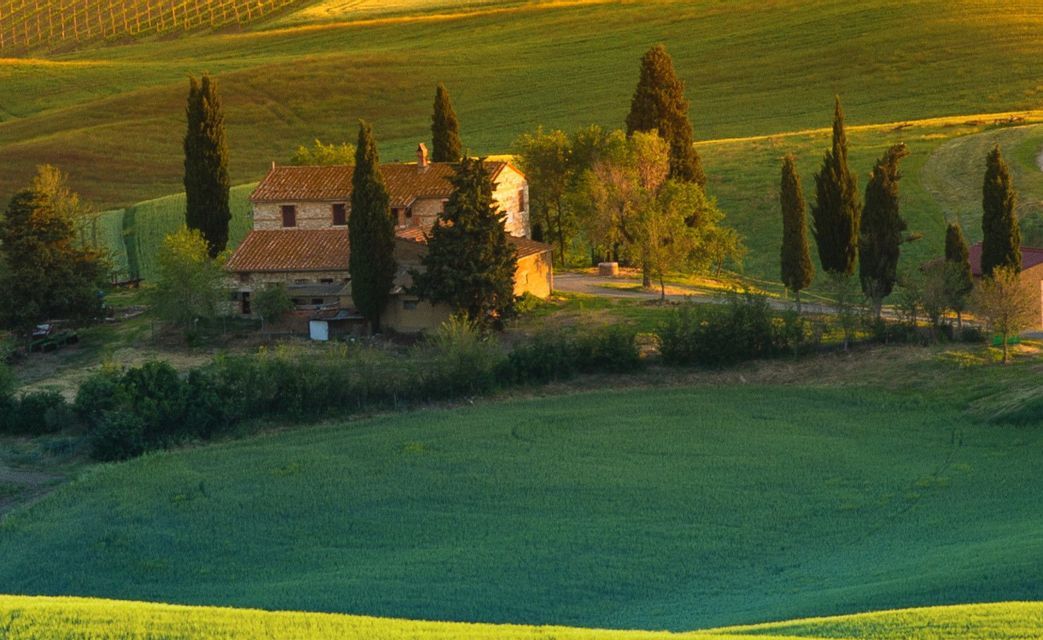 Un casale in pietra con tetto in tegole è circondato da cipressi su una dolce collina verdeggiante durante l'ora d'oro.