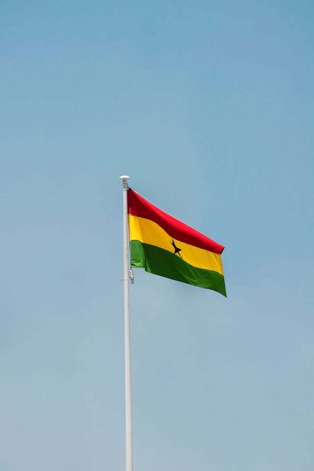 La bandiera del Ghana sventola su un'asta bianca contro un cielo azzurro sereno.