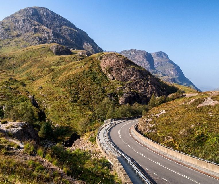 Eine malerische Straße, die sich an einem klaren Tag durch einen grünen Bergpass schlängelt.