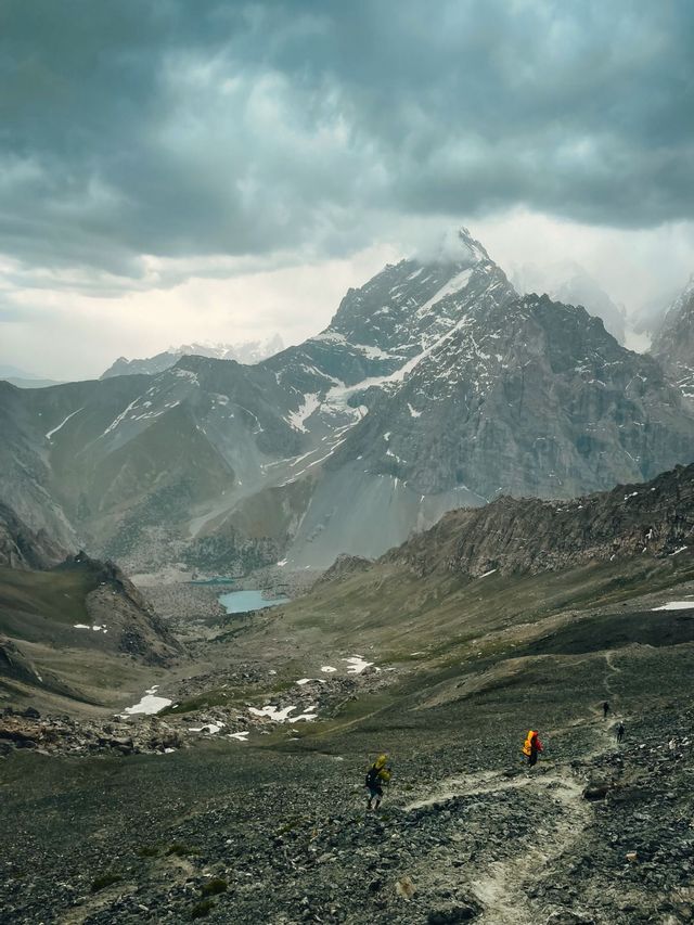 Trekking di gruppo WeRoad lungo un sentiero roccioso in una vasta valle di montagna con un lago sottostante.