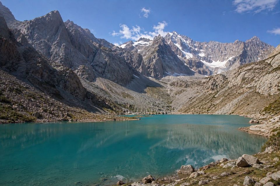 Un lago alpino turchese è circondato da montagne rocciose e innevate, che si riflettono nell'acqua limpida.